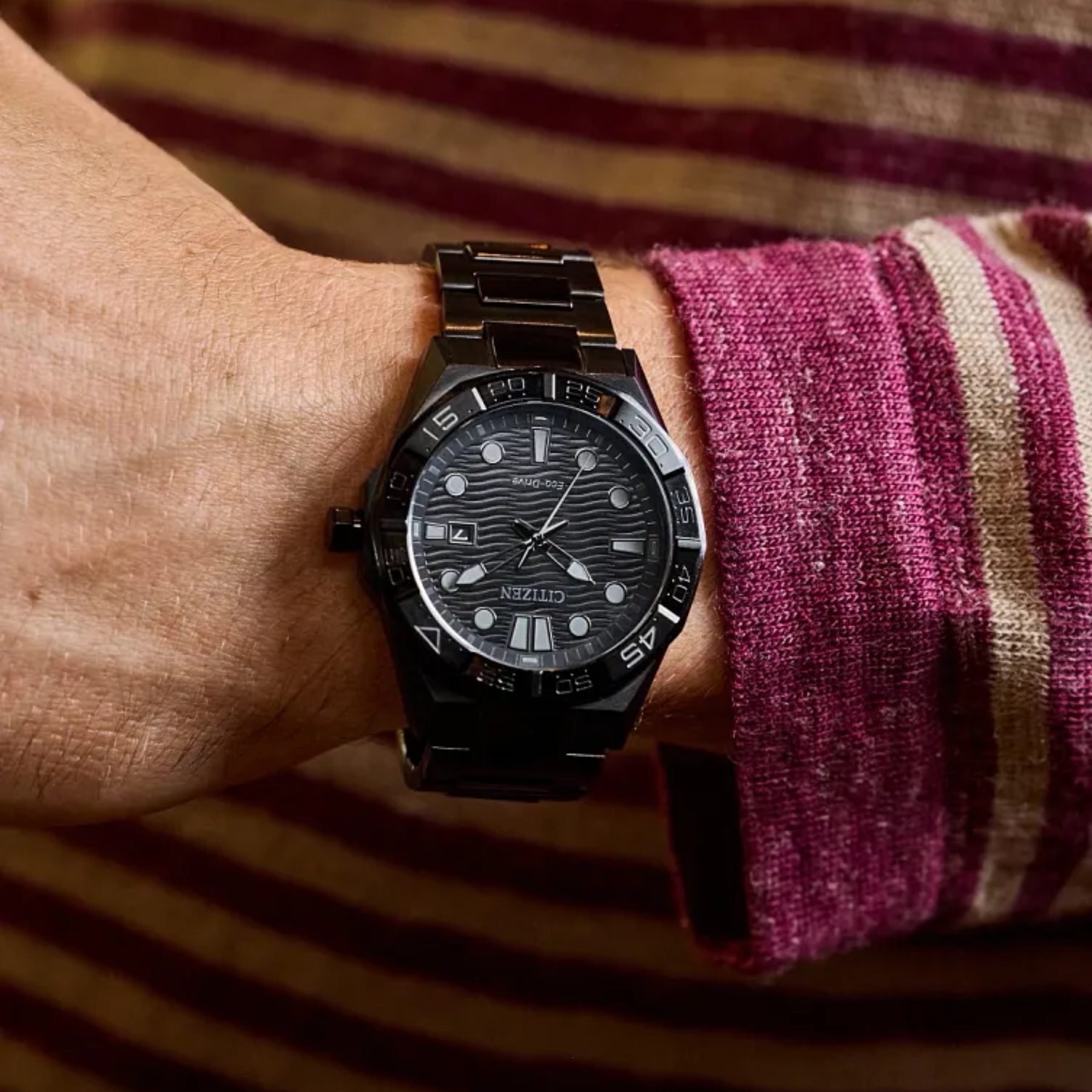 Black wristwatch on a person's wrist with a striped background
