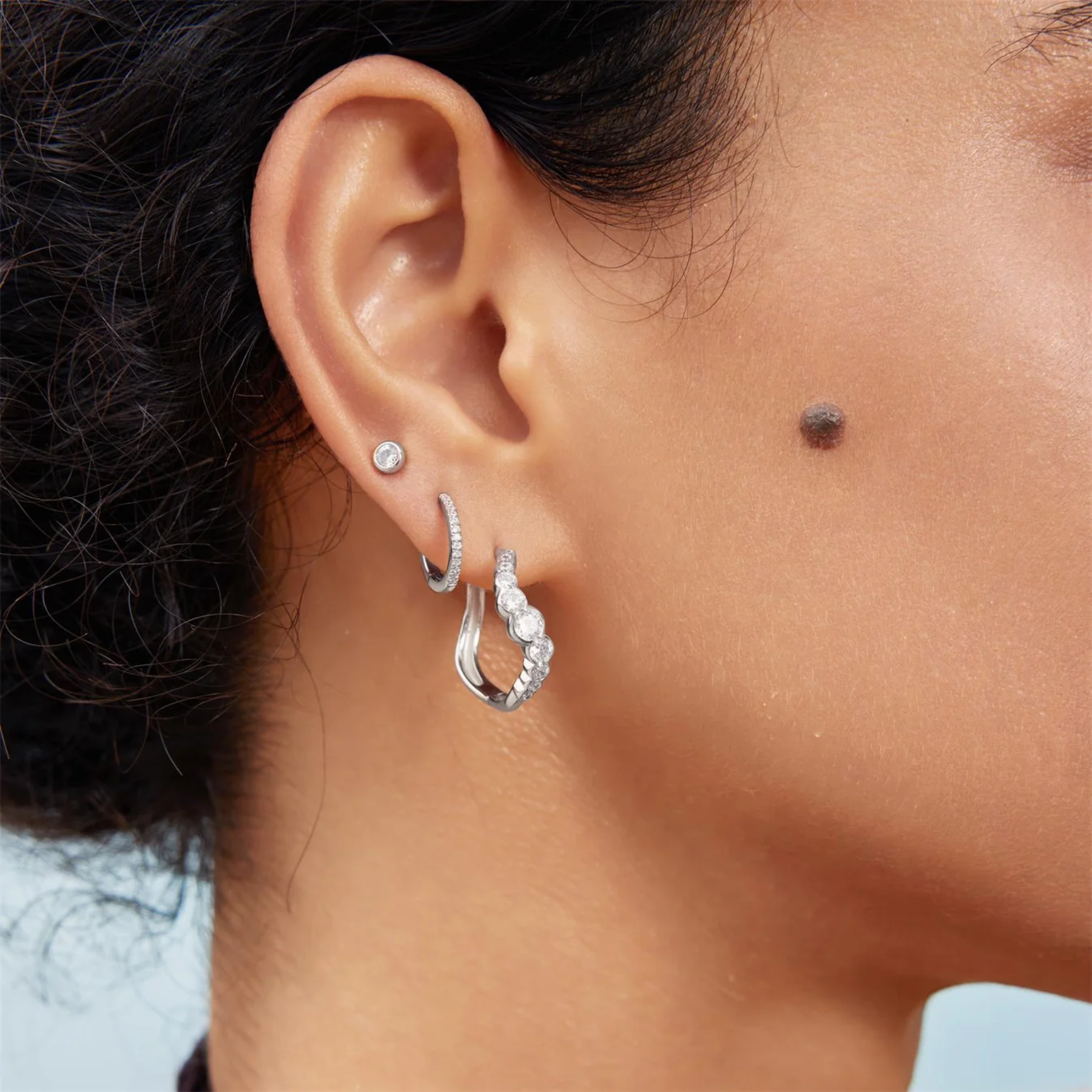 Close-up of an ear wearing silver hoop earrings with a blurred background