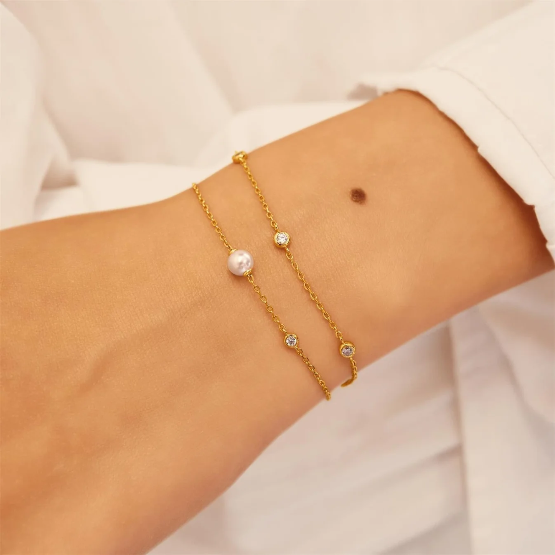 Gold bracelet with pearls and crystals on a wrist against a white background