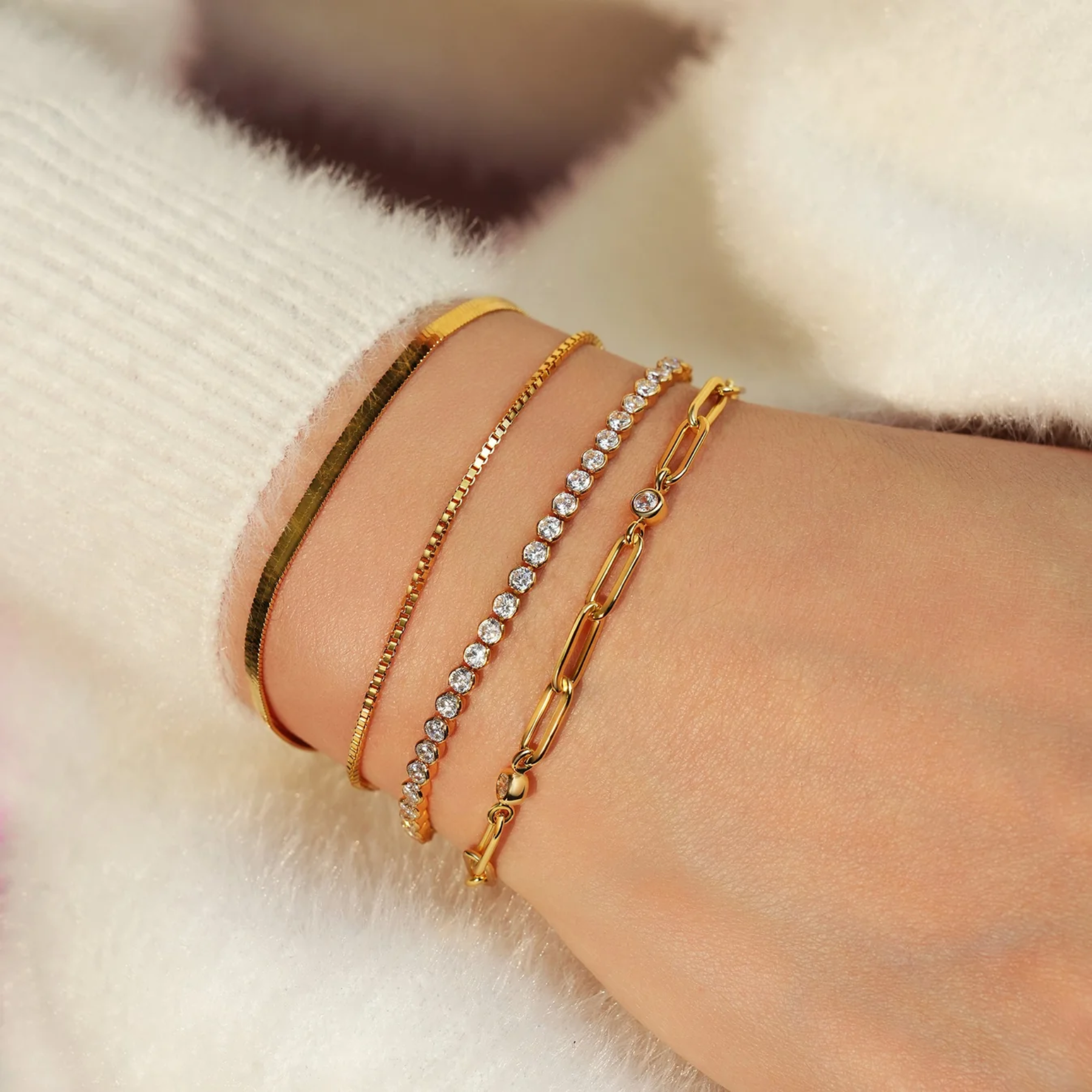 Close-up of a wrist wearing multiple gold bracelets on a soft white background