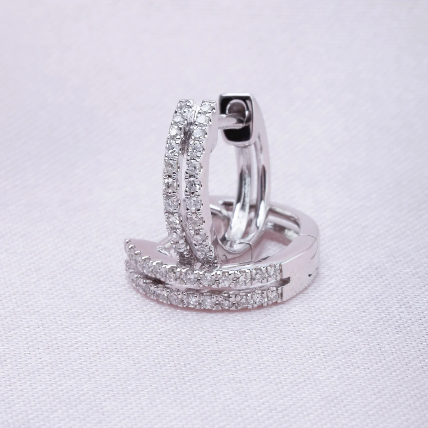 Pair of silver hoop earrings with clear gemstones on a light gray background