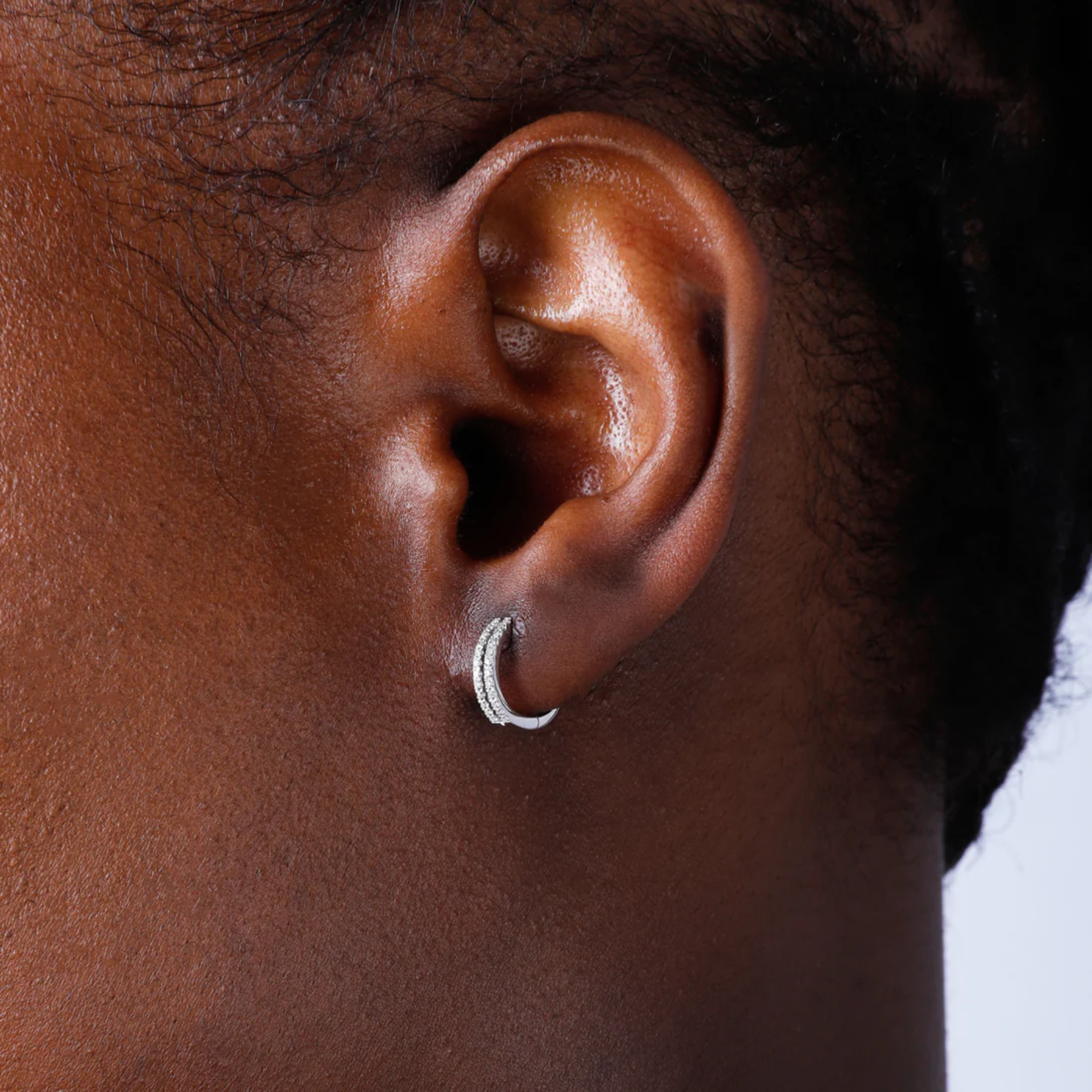 Close-up of an ear wearing a silver hoop earring on a neutral background