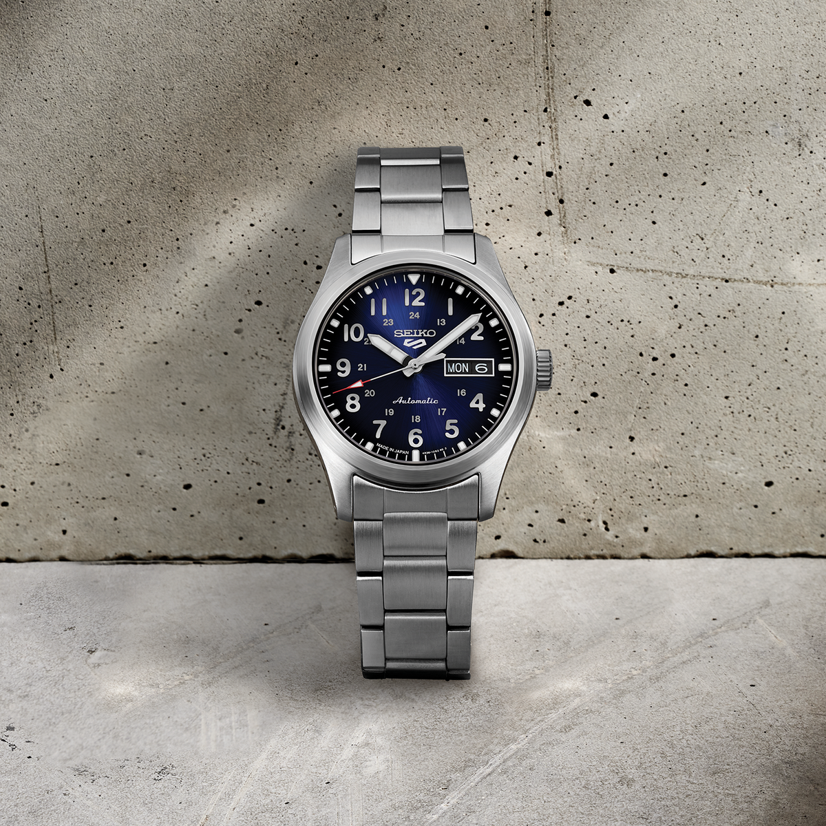 SEIKO SRPG29 blue-dial automatic watch with stainless steel bracelet displayed against a textured concrete background.