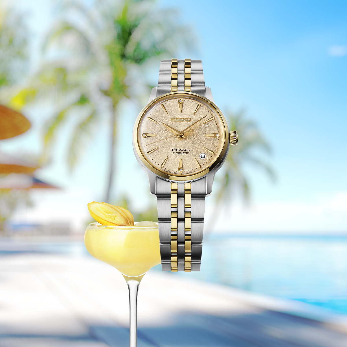 SEIKO SRPL64 two-tone Presage Cocktail Time watch displayed beside a frozen banana cocktail against a tropical poolside background.